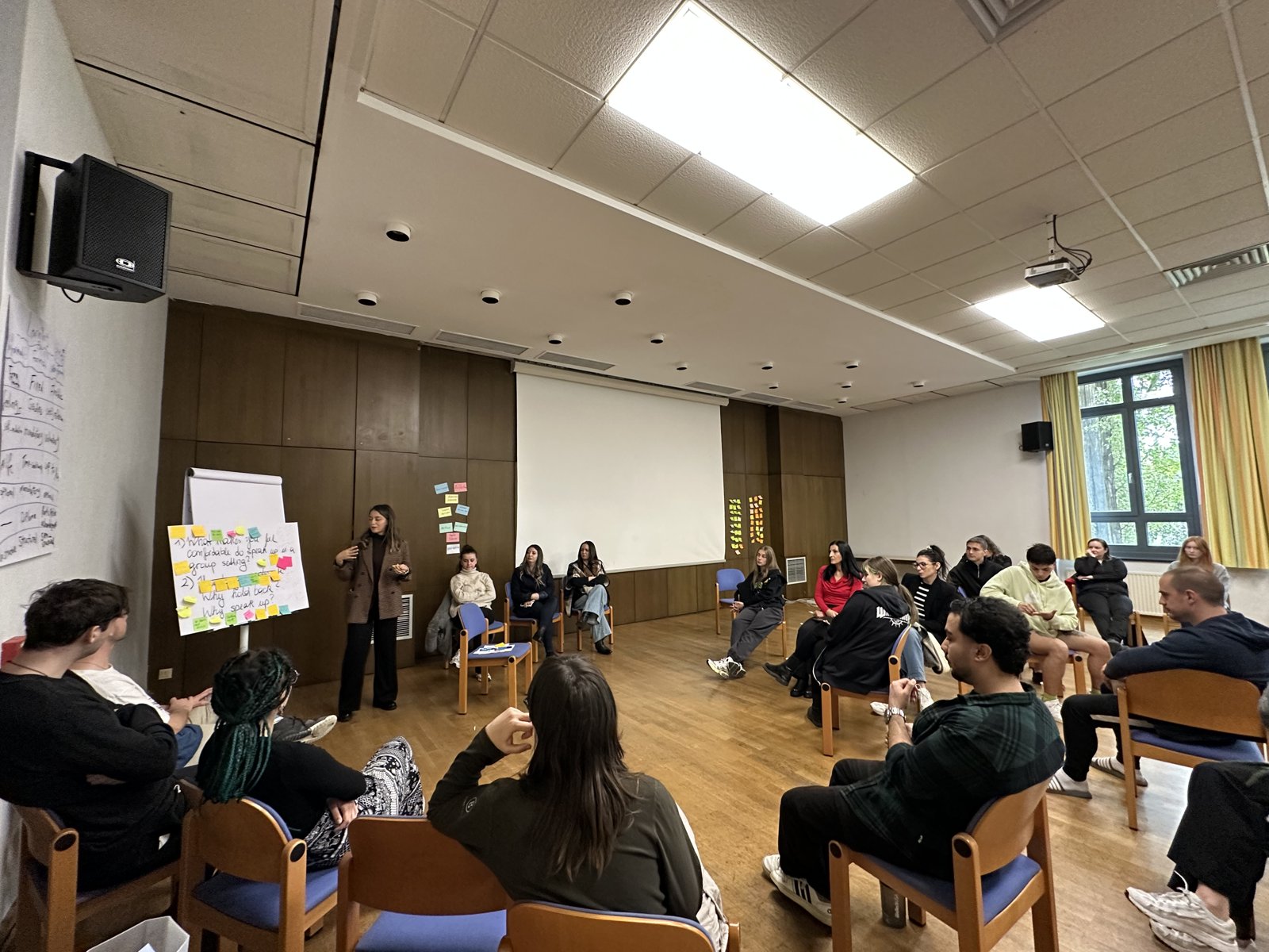 Participants sitting in a large circle in a seminar hall while a facilitator speaks