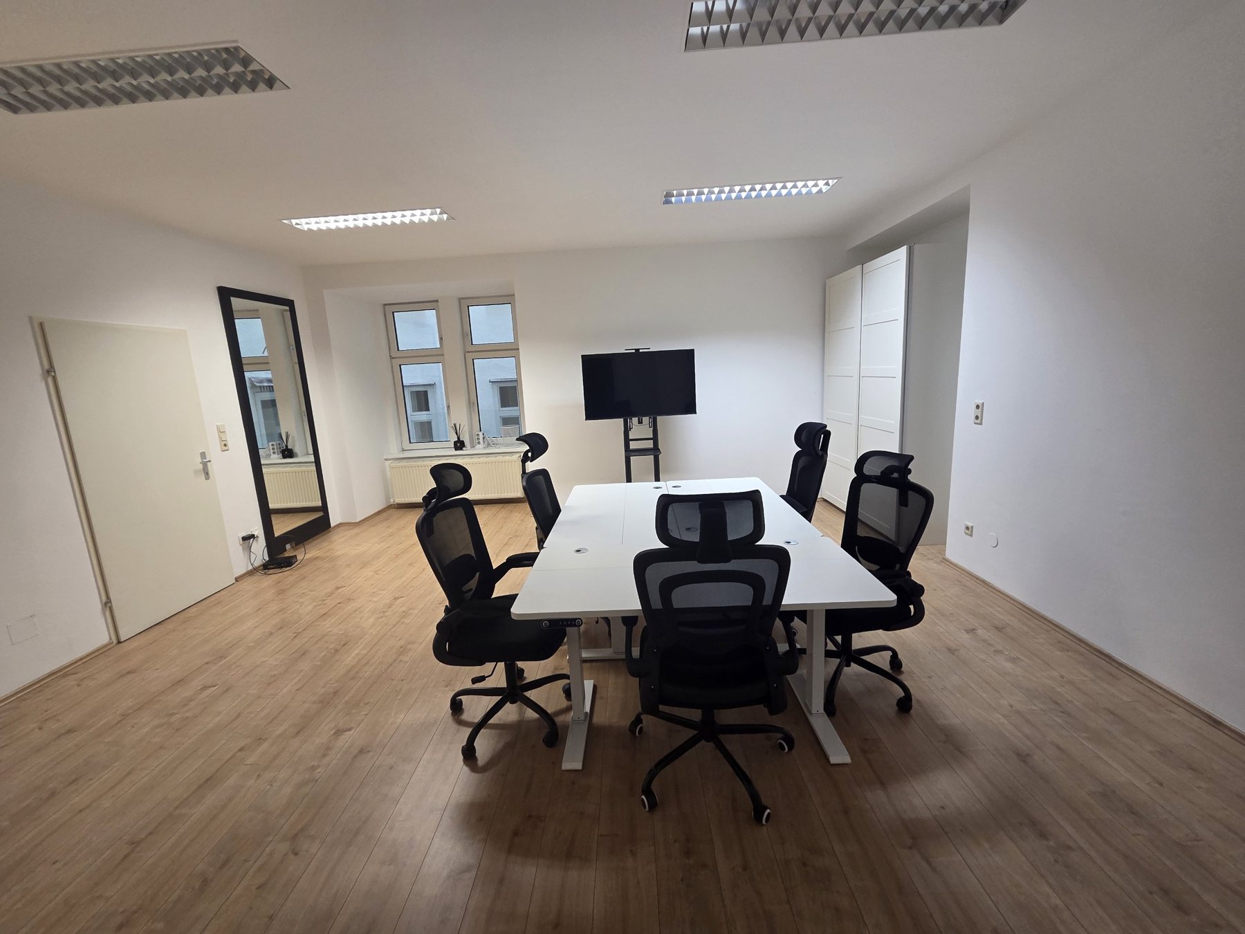 The workspace with white desks, ergonomic chairs, a screen and a large mirror